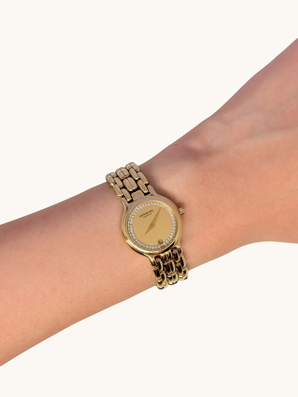 By the Hour vintage gold-tone Raymond Weil Fidelio watch with diamond bezel and gold-plated linked bracelet on a wrist.